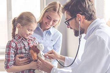 Doctor putting stethoscope on a toy bear being held by a kid